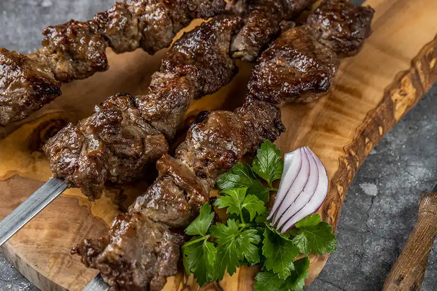 Lamm-Schaschlik Original Nahaufnahme serviert auf einem Holzbrett, angerichtet mit Petersilie und roten Zwiebeln.