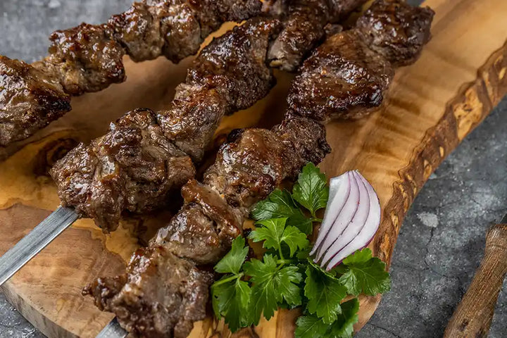 Lamm-Schaschlik Original Nahaufnahme serviert auf einem Holzbrett, angerichtet mit Petersilie und roten Zwiebeln.