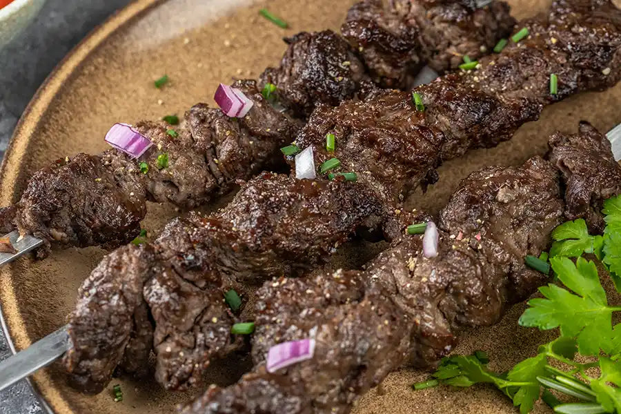 Rindfleisch Schaschlik nach Original Rezept garniert mit roten Zwiebeln, Schnittlauch und Petersilie. Angerichtet auf einem Teller.