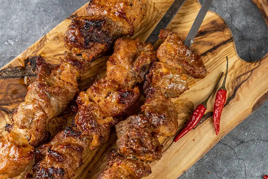 Schweine-Schaschlik Chili auf einem Holzbrett angerichtet mit Chilischoten.