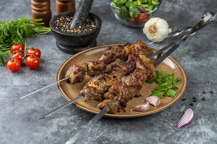 Schweine-Schaschlik Knoblauch-Pfeffer auf einem rustikalen Teller serviert. Garniert mit Petersilie und Knoblauch. Dekoriert mit buntem Pfeffer, Knoblauch, roten Zwiebeln, Salat und Cocktail-Tomaten.