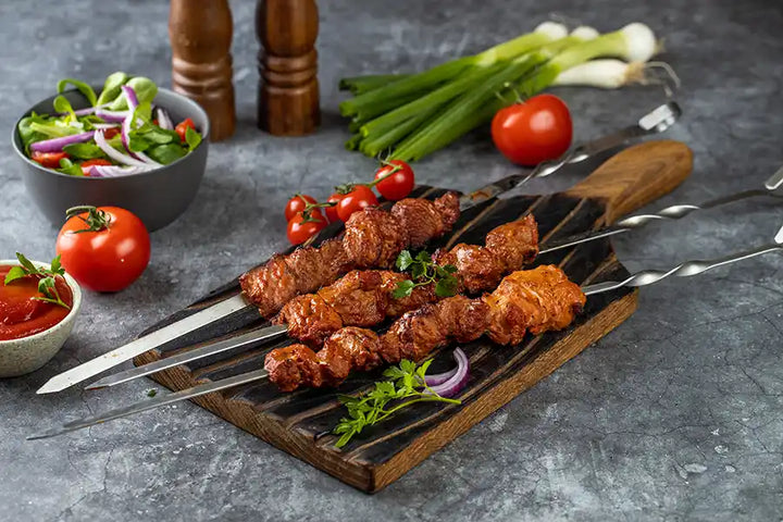 Schweine-Schaschlik Tomate angerichtet auf einem rustikalen Holzbrett mit roten Zwiebeln und Petersilie. Dekoriert mit Frühlingszwiebeln, Tomate, Sosse, Pfeffer- und Salzmühle aus Holz und Salat.