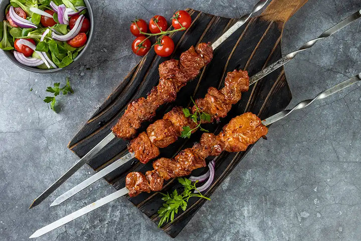 Schweine-Schaschlik Tomate angerichtet auf einem rustikalen Holzbrett mit roten Zwiebeln und Petersilie. Dekoriert mit Cocktail-Tomaten und Salat.