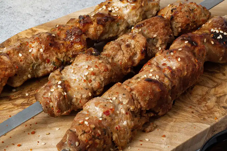 Schweine-Schaschlik Yakusa angerichtet auf einem Holzbrett. Garniert mit Sesam und Chili.